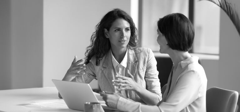 SINGLE-IMAGE_two-business-women-sit-at-desk-laptop_jul24
